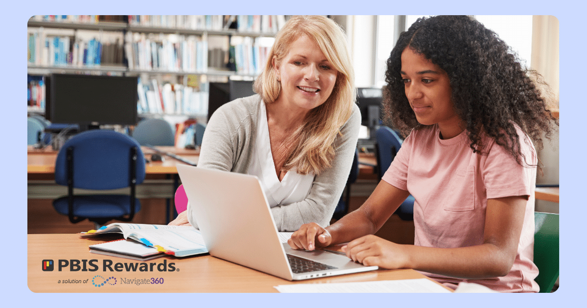 Young student on laptop in classroom with her teacher.
